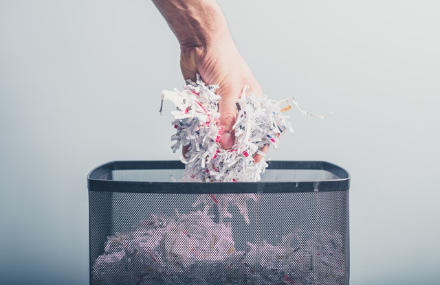 foto de mão jogando papel triturado no lixo